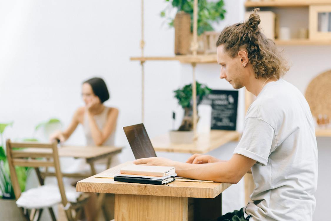 Person with a bun hairstyle studying on a laptop in a bright cafe.