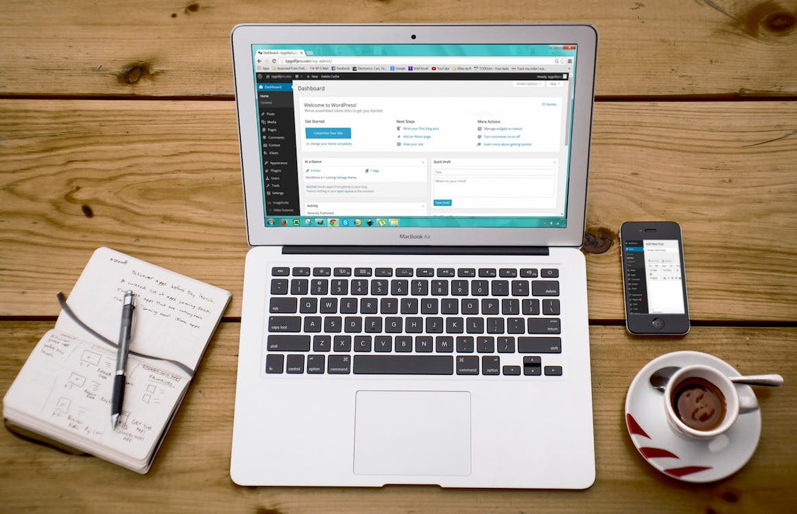 Free Turned-on Macbook Air Beside Black Iphone 4, Cup of Tea, and Notebook on Brown Wooden Surface Stock Photo