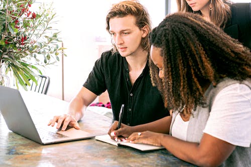 Free Man Working on Laptop while Woman Takes Notes Stock Photo