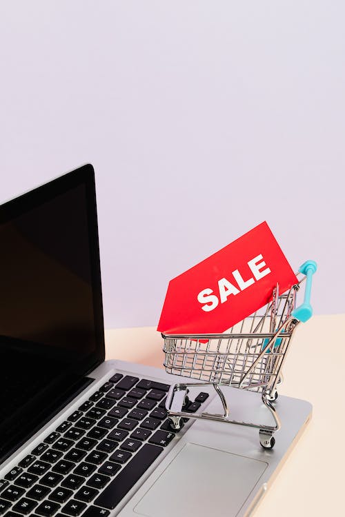 Free A Red Sale Tag on a Miniature Shopping Cart Placed on a Macbook Laptop Stock Photo