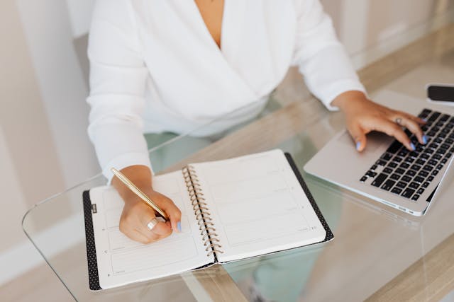 Woman writing on a notebook with a laptop