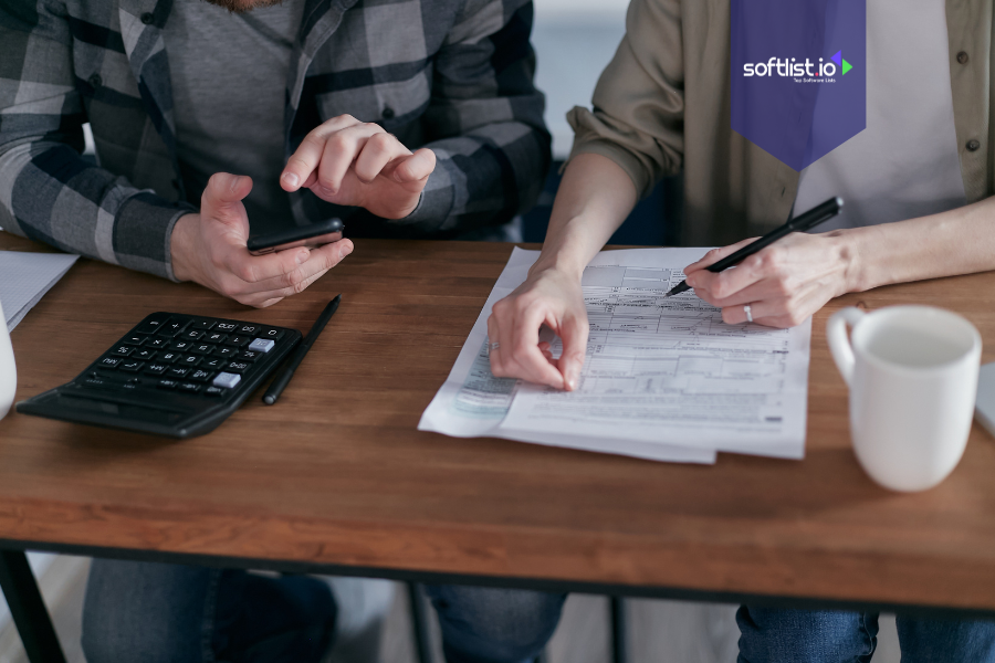 Two people reviewing tax documents with a calculator and smartphone, representing tax implications of selling an online business.