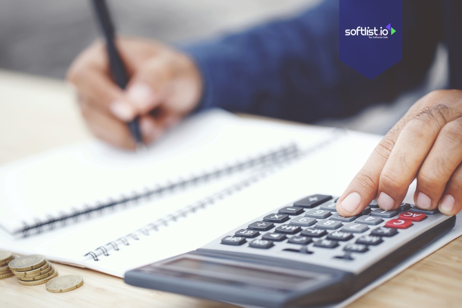 Close-up of a person using a calculator and writing in a notebook with coins nearby, symbolizing tax implications of selling an online business.