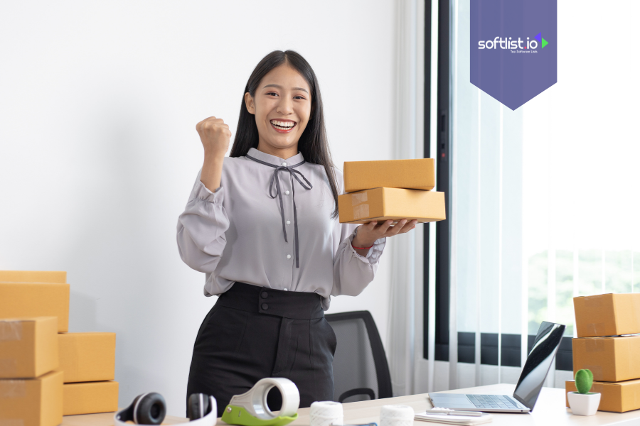 Smiling businesswoman holding shipping boxes in an office, representing success and awareness of tax implications of selling an online business.