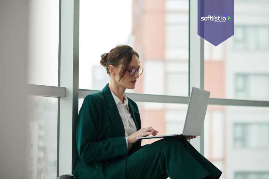 Businesswoman in a green suit working on a laptop by the window, symbolizing buying an online business as an individual.