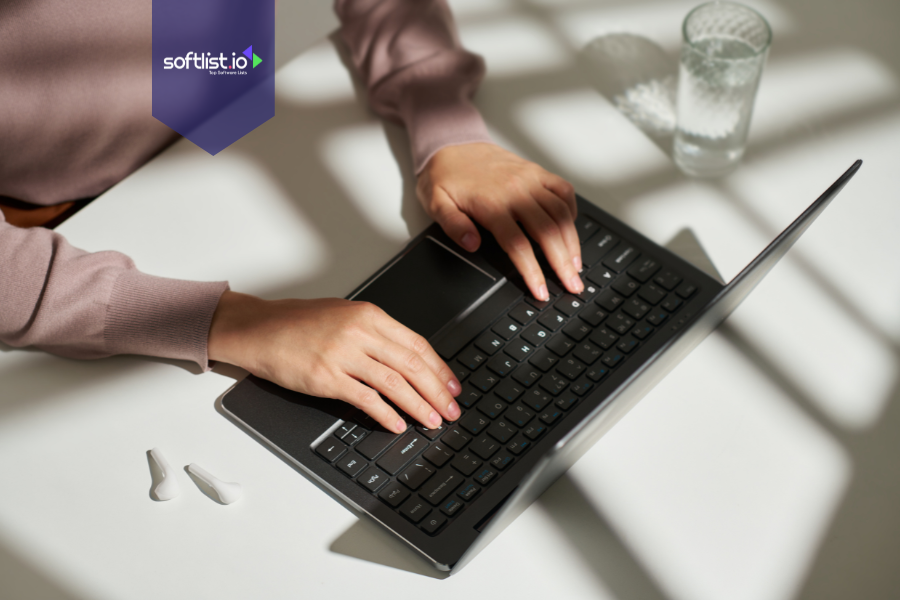 Close-up of a person typing on a laptop with earbuds and a glass of water on the table, representing buying an online business as an individual.