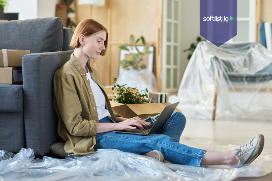 Young woman sitting on the floor with a laptop among moving boxes, symbolizing buying an online business as an individual.