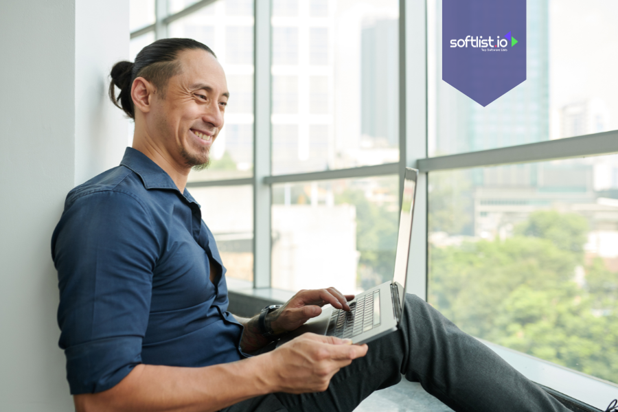 Smiling man sitting by a window using a laptop, representing buying an online business as an individual.