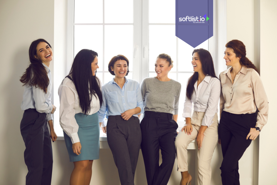 Group of professional women laughing and connecting by a window, representing community-driven business valuation through trust and team engagement.